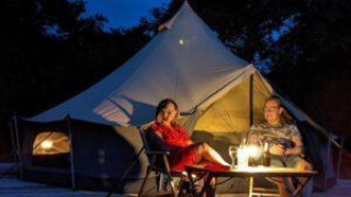 Zwei Personen entspannen vor einem beleuchteten Luxe-Bellzelt auf CharmeCamping De Regge-Vallei, Niederlande.