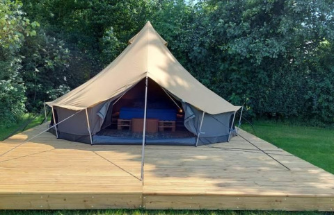 Luxe belltent on a wooden deck at CharmeCamping De Regge-Vallei, Netherlands, surrounded by lush greenery.