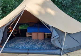 Indretning af en luksuriøs belltent med seng, tæppe og møbler i CharmeCamping De Regge-Vallei, Holland.