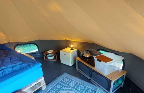 Innenansicht eines Luxus-Bellzeltes mit Bett, Minikühlschrank und Küchenutensilien bei CharmeCamping De Regge-Vallei.
