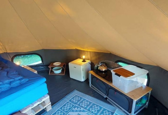 Interior acogedor de una tienda tipi de lujo con cama, mini nevera y utensilios de cocina en CharmeCamping De Regge-Vallei.