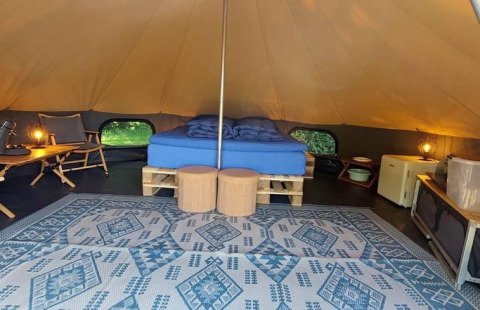 Innenaufnahme eines luxuriösen Belltents mit Doppelbett, Teppich und Möbeln bei CharmeCamping De Regge-Vallei, Niederlande.