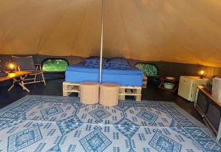 Indretning af luksus belltelt med dobbeltseng, tæppe, borde og stole på CharmeCamping De Regge-Vallei, Holland.