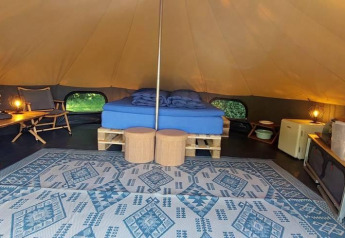 Indretning af luksus belltelt med dobbeltseng, tæppe, borde og stole på CharmeCamping De Regge-Vallei, Holland.