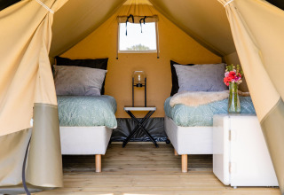 Interior de una tienda safari con dos camas, suelo de madera y flores en CharmeCamping De Regge-Vallei, Países Bajos.