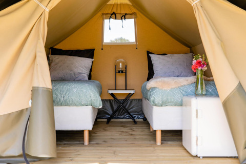 Interior de una tienda safari con dos camas, suelo de madera y flores en CharmeCamping De Regge-Vallei, Países Bajos.