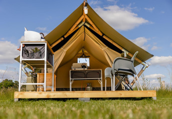 Foto di una tenda safari su una piattaforma di legno con sedie, tavolo e attrezzatura da campeggio.