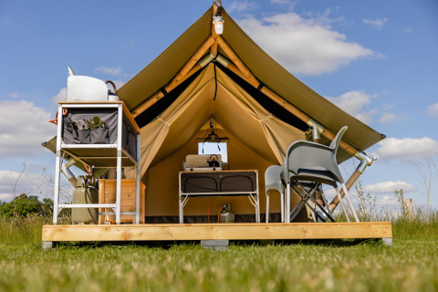 Foto van een safaritent op een houten platform met stoelen, tafel en kampeergerief onder openlucht.