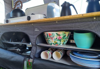 Kleurrijke kommen en servies in een safari tentkeuken, met fornuis en waterkoker op het aanrecht.