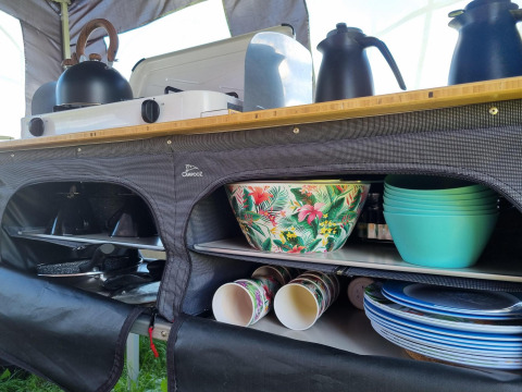 Colorful bowls, cups, and kitchenware organized in a safari tent kitchen with stove and kettle on top.