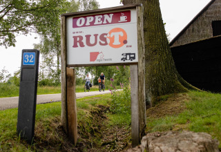 Panneau devant une tente safari au CharmeCamping De Regge-Vallei, Pays-Bas, des cyclistes à l’arrière-plan.