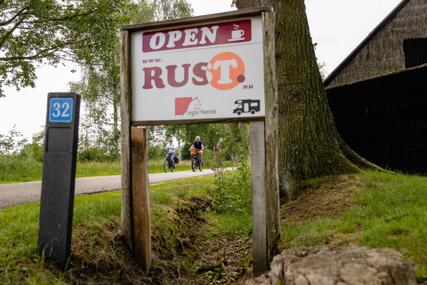Panneau devant une tente safari au CharmeCamping De Regge-Vallei, Pays-Bas, des cyclistes à l’arrière-plan.