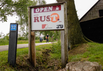 Panneau devant une tente safari au CharmeCamping De Regge-Vallei, Pays-Bas, des cyclistes à l’arrière-plan.