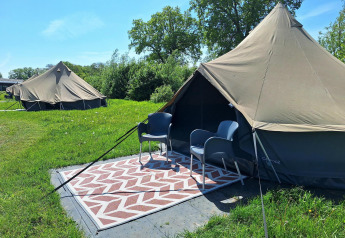 Zwei Safari-Zelte mit Stühlen und Teppich davor auf einer grünen Wiese bei CharmeCamping De Regge-Vallei.