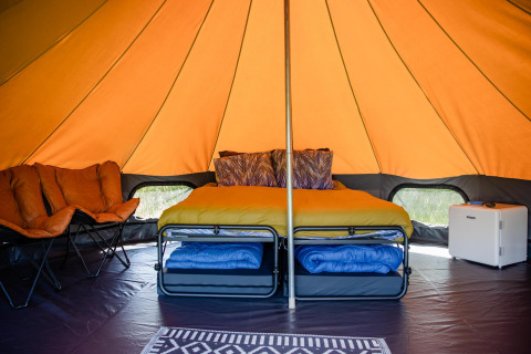 Interior de una tienda de safari glamping en los Países Bajos con cama, asientos y minibar visible.