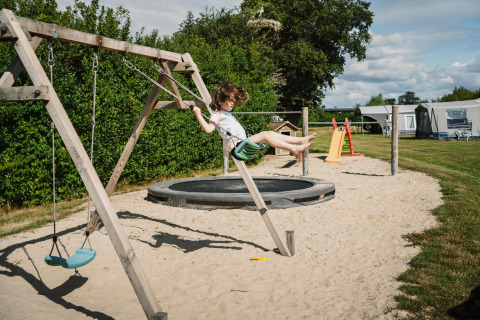 Kind schaukelt auf dem Spielplatz mit Sand bei Glamping Belltent auf CharmeCamping De Regge-Vallei, Niederlande.
