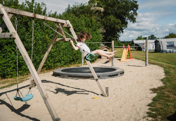 Enfant se balançant sur une aire de jeux sablée au Glamping belltent, CharmeCamping De Regge-Vallei, Pays-Bas.