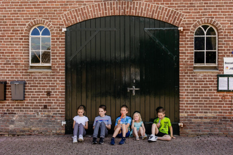 Cinq enfants assis devant une grande porte de grange au Glamping belltent, CharmeCamping De Regge-Vallei, Pays-Bas.
