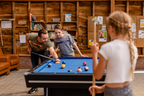 Een man en twee kinderen spelen samen biljart in de gezellige lounge van CharmeCamping De Regge-Vallei.