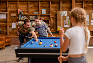 En mand og to børn spiller billard sammen i en hyggelig opholdsstue på CharmeCamping De Regge-Vallei.