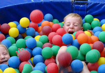Due bambini ridono e giocano nella vasca di palline colorate al Glamping belltent di CharmeCamping De Regge-Vallei.