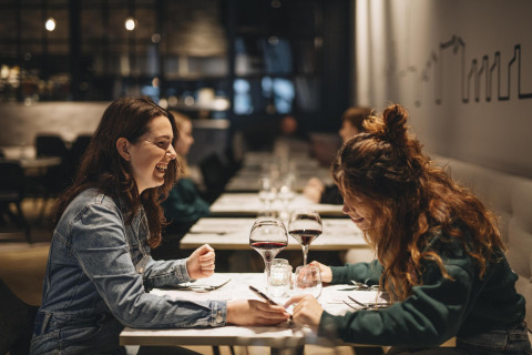 Twee vrouwen lachen samen en drinken wijn aan een sfeervol gedekte tafel in een modern restaurant.