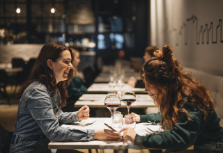 Twee dames lachen en genieten van rode wijn aan een gezellige tafel in een stijlvol restaurant.