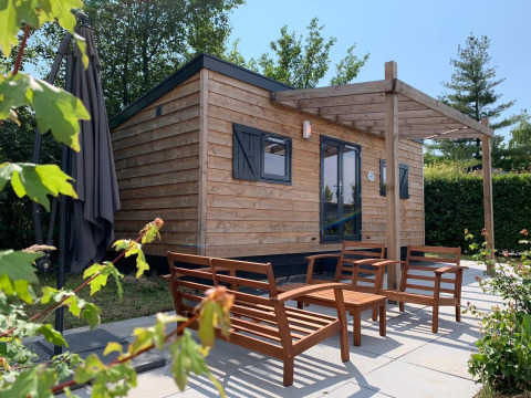 Pequeña casa de madera con asientos exteriores en Holiday Park Mölke, Países Bajos, rodeada de naturaleza.