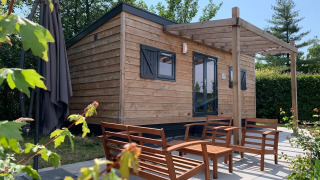 Wooden tiny house with outdoor seating at Holiday Park Mölke, Netherlands, surrounded by greenery.