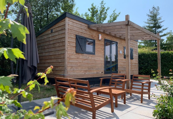 Kleine houten woning met terrasmeubilair bij Holiday Park Mölke in Nederland, omringd door groen.