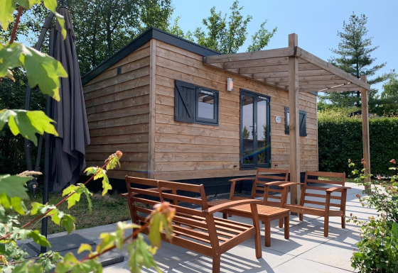 Pequeña casa de madera con asientos exteriores en Holiday Park Mölke, Países Bajos, rodeada de naturaleza.