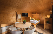Interior de una tiny house acogedora, con paredes de madera, mesa redonda y cama en Holiday Park Mölke.
