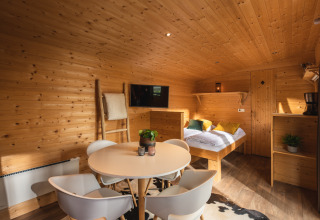 Interior de una tiny house acogedora, con paredes de madera, mesa redonda y cama en Holiday Park Mölke.
