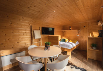 Interior de una tiny house acogedora, con paredes de madera, mesa redonda y cama en Holiday Park Mölke.