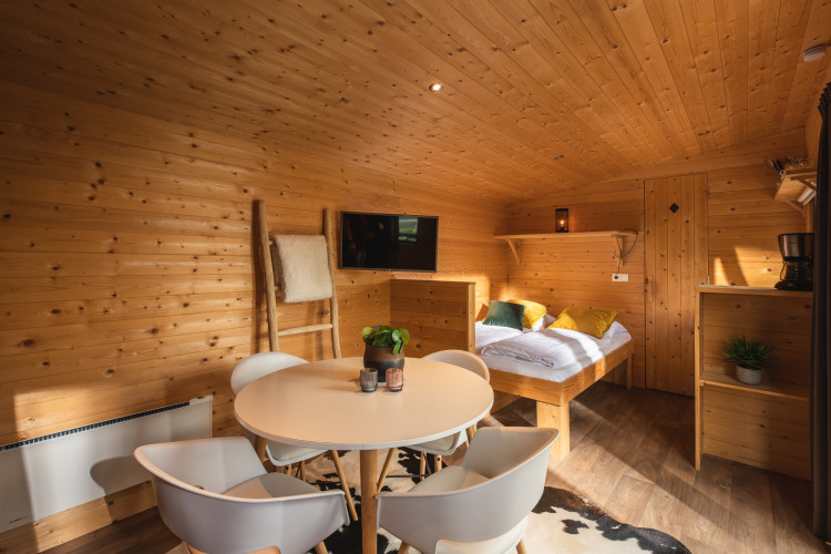 Interior de una tiny house acogedora, con paredes de madera, mesa redonda y cama en Holiday Park Mölke.