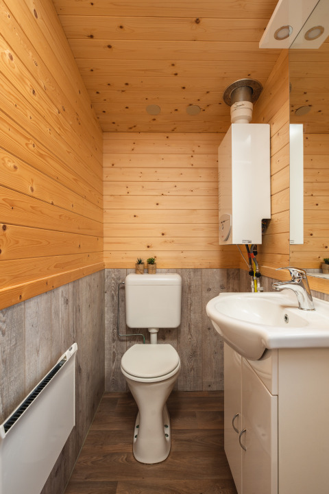 Baño pequeño en una tiny house con paneles de madera, inodoro blanco y lavabo, Tiny House en Holanda.