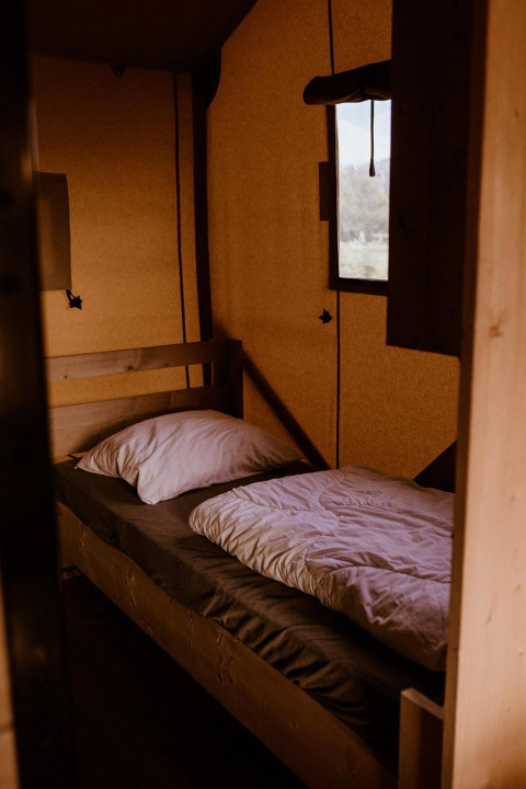 Letto singolo con biancheria bianca in una tenda safari a Groupaccommodation 'de Blokhut', Paesi Bassi.