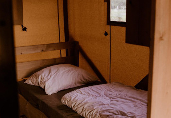 Ein einfaches Bett mit weißer Bettwäsche in einem Safarizelt im Holiday Park Eigen Wijze, Niederlande.