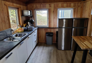 Modern kitchen area with wood paneling, two fridges, a sink, and large windows in a Dutch safari tent.