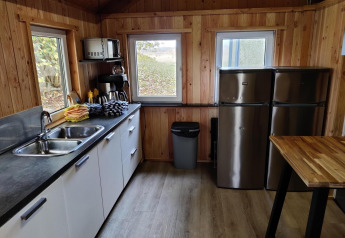 Modern kitchen area with wood paneling, two fridges, a sink, and large windows in a Dutch safari tent.
