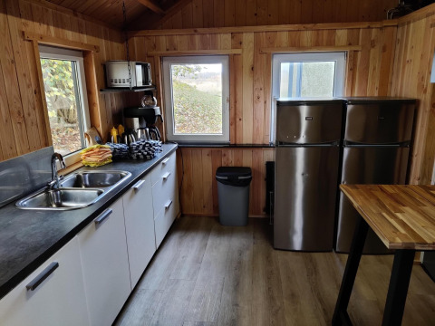 Modern kitchen area with wood paneling, two fridges, a sink, and large windows in a Dutch safari tent.