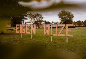 Panneau en bois 'EIGEN WIJZE' sur une pelouse au parc de vacances Eigen Wijze, aux Pays-Bas, tentes visibles.