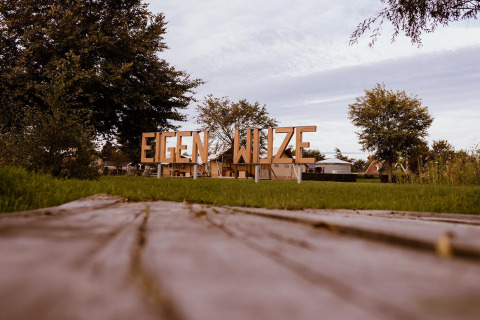 Foto del letrero 'EIGEN WIJZE' en el parque de vacaciones Eigen Wijze en los Países Bajos con árboles al fondo.