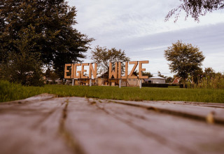 Foto del letrero 'EIGEN WIJZE' en el parque de vacaciones Eigen Wijze en los Países Bajos con árboles al fondo.