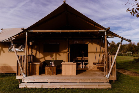 Foto af glamping-indkvartering med et telt og træveranda med udendørsmøbler i landlige omgivelser.