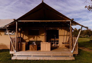 Foto af glamping-indkvartering med et telt og træveranda med udendørsmøbler i landlige omgivelser.