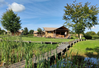 Tentes safari et cabanes au Holiday park Eigen Wijze, Pays-Bas, sous un ciel bleu et arbres verdoyants.