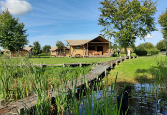 Safari-telte ved Groupaccommodation 'de Blokhut' på Holiday park Eigen Wijze, omgivet af grønt og sø.