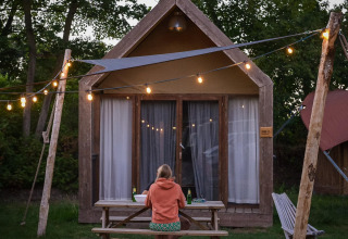 Persona sentada en una mesa frente a una tiny house Boutique suite en Holiday Park Mölke, Países Bajos, con luces decorativas.
