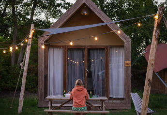 Persona sentada en una mesa frente a una tiny house Boutique suite en Holiday Park Mölke, Países Bajos, con luces decorativas.